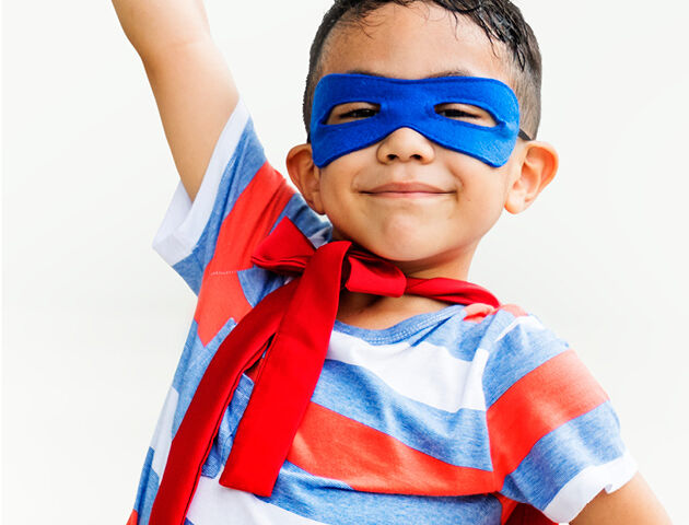 Ein Junge ist als Superman verkleidet und reckt stolz seine Faust in die Luft.